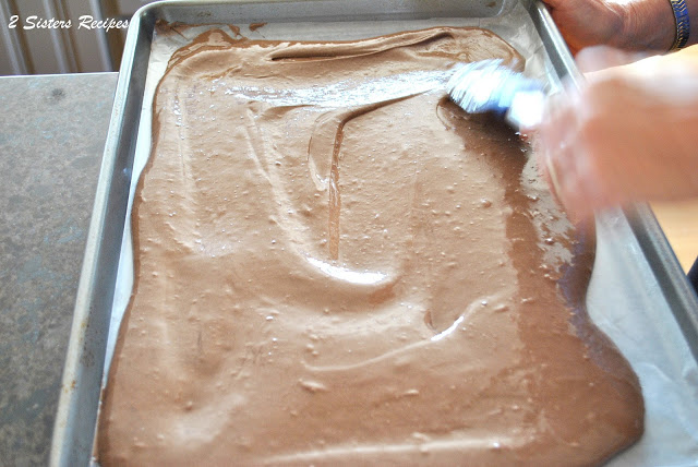 Spreading the chocolate cake batter on a large cookie baking sheet.  by 2sistersrecipes.com 