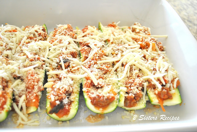 A white baking dish with raw zucchini boats filled with sauce and shredded mozzarella on top. 