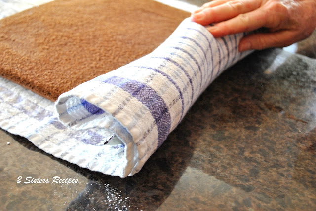 A kitchen towel rolling up a chocolate sheet cake. by 2sistersrecipes.com