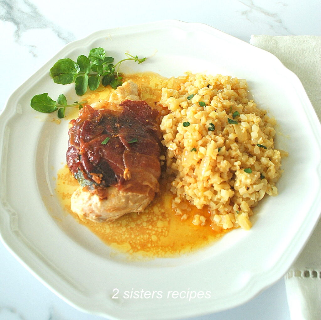 A white dinner plate with a grilled chicken wrapped with crispy prosciutto and cauliflower rice on the side.