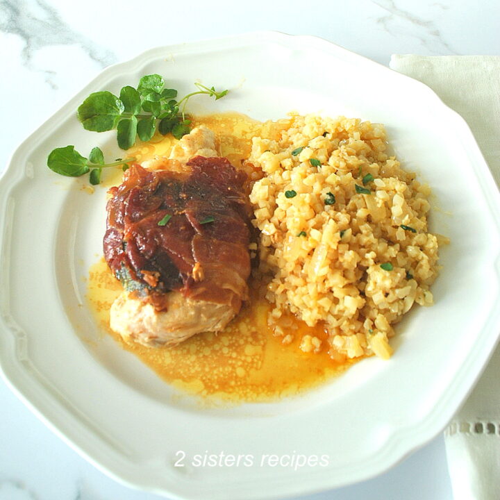 A white dinner plate with a grilled chicken wrapped with crispy prosciutto and cauliflower rice on the side.