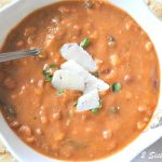 A bowl of creamy bean soup with parmesan shavings on top and a spoon inside the bowl.