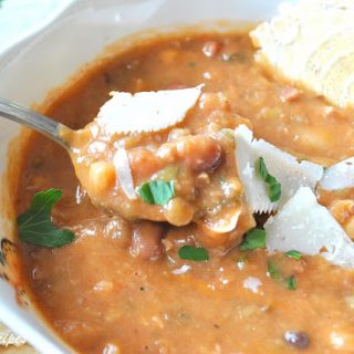 A bowl of bean soup with a spoonful and a cracker in the soup.