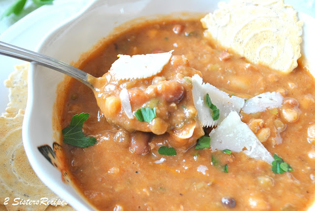 A bowl of bean soup with a spoonful and a cracker in the soup.