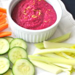 Beet Hummus served on a white platter with fresh veggie sticks.