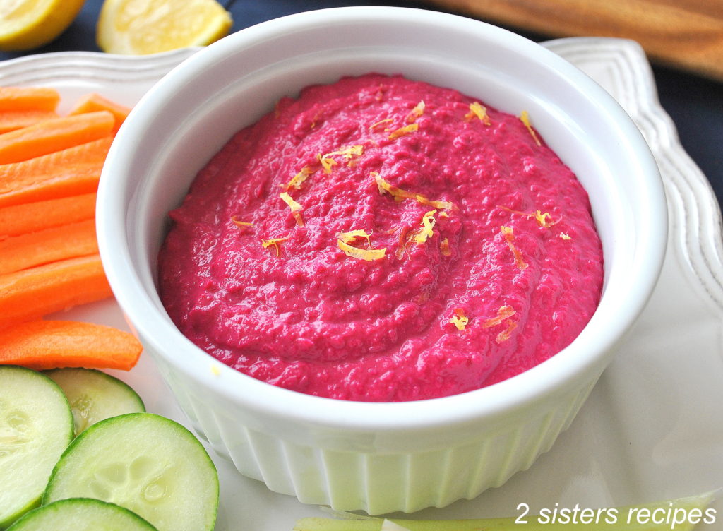 A white bowl filled with beet hummus and fresh veggies on the side,