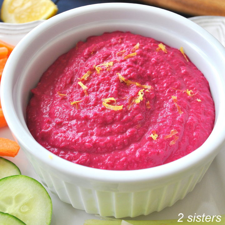 A white bowl filled with beet hummus and fresh veggies on the side,