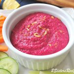A white bowl filled with beet hummus with veggies on the side.
