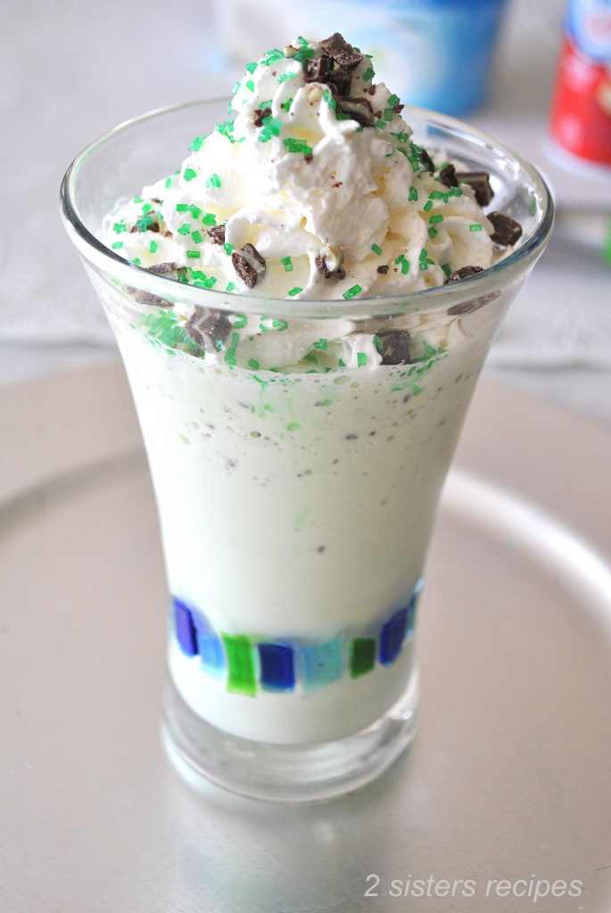 A tall glass filled with a milkshake made with ice cream, and topped with whipped cream and green mint candies.