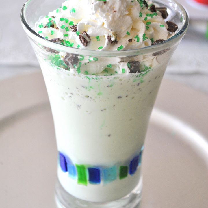 A tall glass filled with a milkshake made with ice cream, and topped with whipped cream and green mint candies.