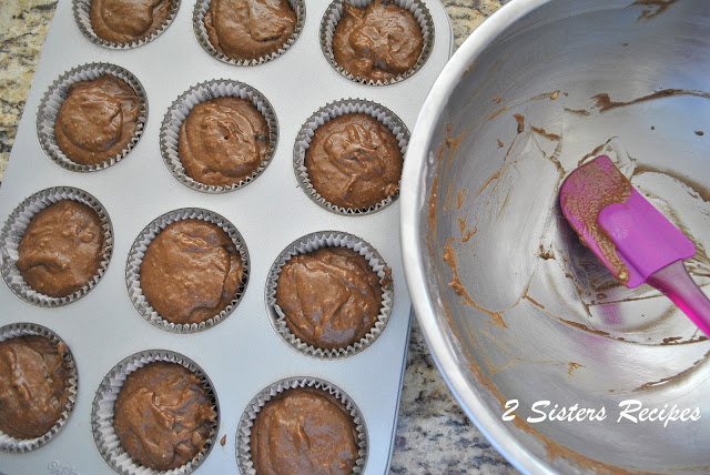 One silver mixing bowl with spatula, and muffin pan filled with chocolate mixture. by 2sistersrecipes.com