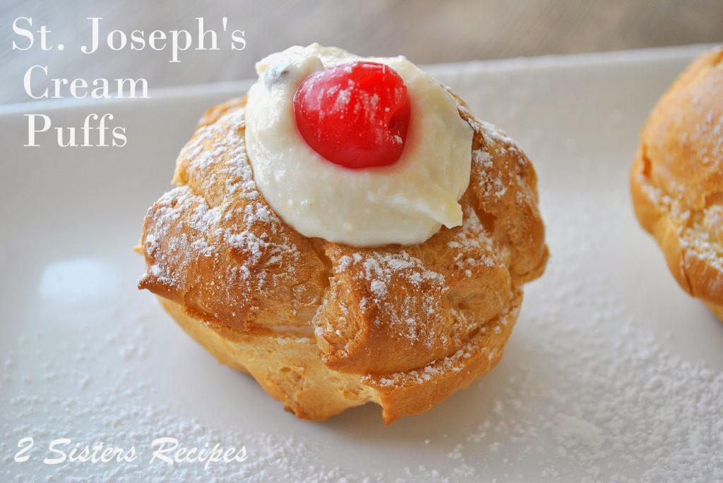 A cream puff placed on white platter with cream filling and cherry on top.