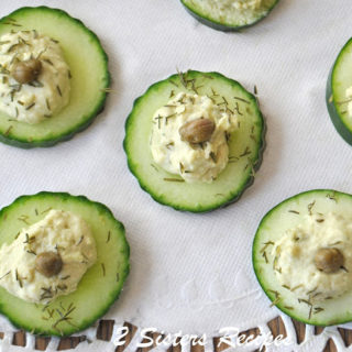 A dolie with cucumber disks topped with some hummus, dill and a caper.