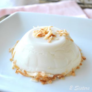 A white pudding molded into a round shape with toasted shredded pudding, served on a white plate.