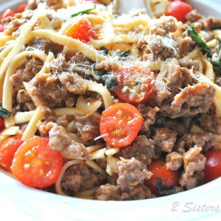 A white plate filled with crumbled sausage, cherry tomatoes and thin noodles.
