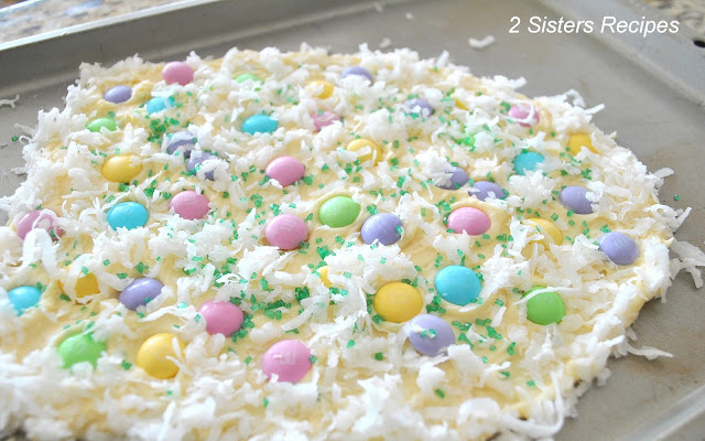 A baking sheet with white chocolate decorated with shredded coconut and pastel colored M&M's. 