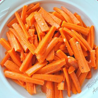 A round white ceramic bowl filled with cooked carrots sticks.