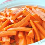 A white ceramic round bowl filled with cooked carrots sticks.