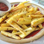 A round plate filled with roasted parsnips and a side of ketchup place on the plate.