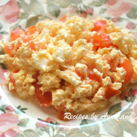 A pink and light green colored plate filled with cooked egg with tomatoes.