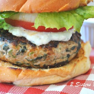 A grilled burger served on a bun with lettuce, tomato and creamy tzatziki sauce.