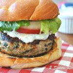 A grilled turkey burger on a bun topped with lettuce, tomato and fresh tzatziki sauce.