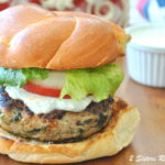 A grilled burger in a hamburger bun topped with lettuce, tomato and creamy sauce.