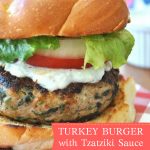 A grilled burger in a bun with lettuce, tomato and creamy tzatziki sauce.