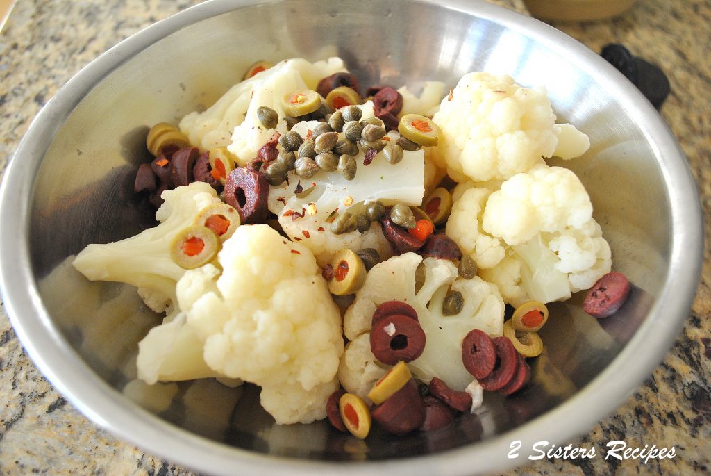 A silver mixing bowl with boiled cauliflower florets, olives, and capers.