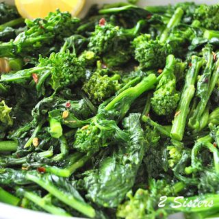 A platter filled with cooked broccoli and a lemon wedge on the side.