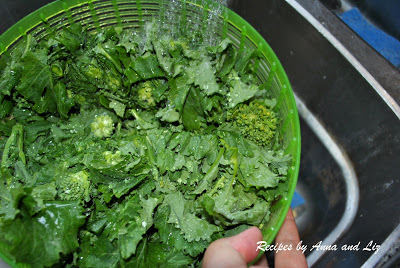 Rinsing the green vegetable in a plastic green colander under running water.
