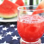 A short glass filled with watermelon juice and a slice of watermelon on the rim of the glass.