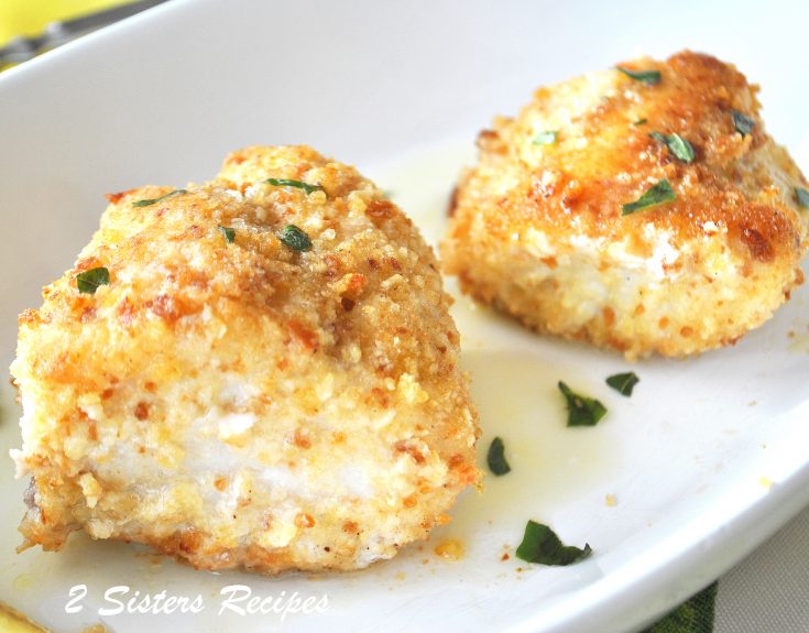 Two pieces of baked fish coated with bread crumbs served on a white plate.