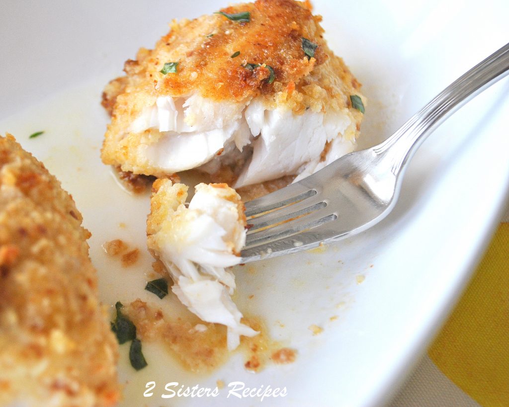  A forkful of cooked white fish over a white plate.