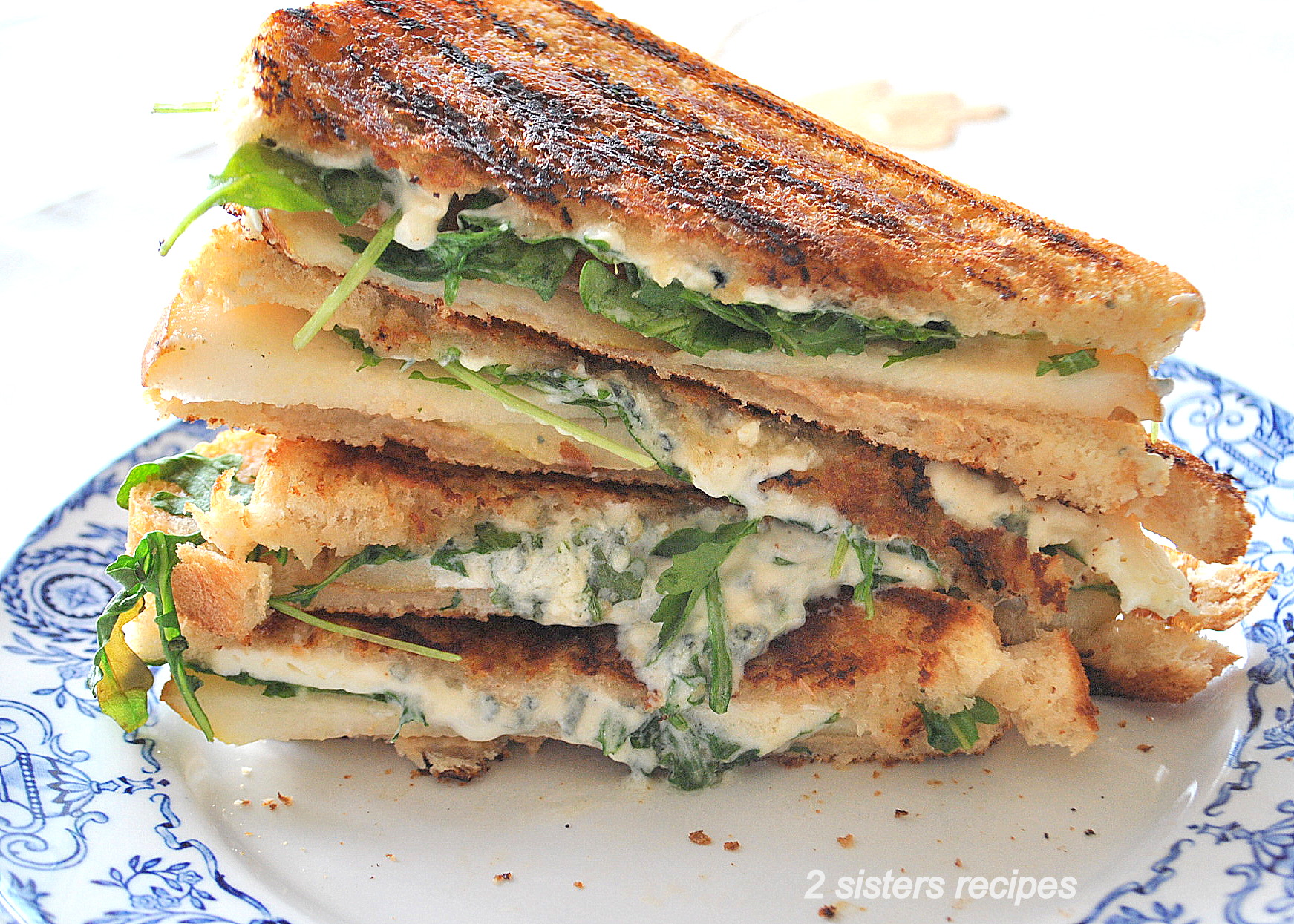 Grilled Cheese and Pear Sandwiches piled on top of one another on a blue and white plate.