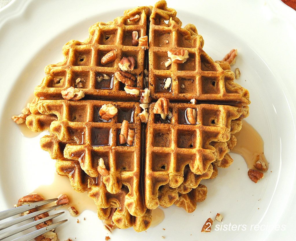pumpkin waffles are served on a white plate with chopped walnuts and maple syrup on top.