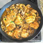 A black skillet with pieces of chicken cooked with Marsala wine and mushrooms.