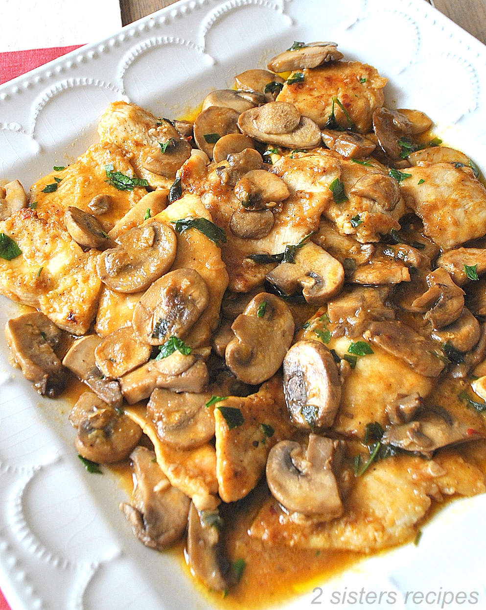 A white platter filled with pieces of cooked chicken and mushrooms in a brown gravy.