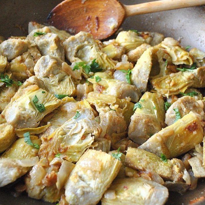 A large skillet filled with sautéed artichoke hearts, parsley and bread crumbs.