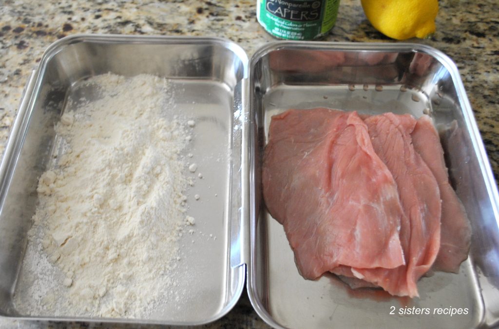 Photo of flour in one tray and raw veal cutlets in the second tray. by 2sistersrecipes.com 