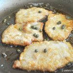 Four pieces of veal are sautéing in a skillet with capers on top.