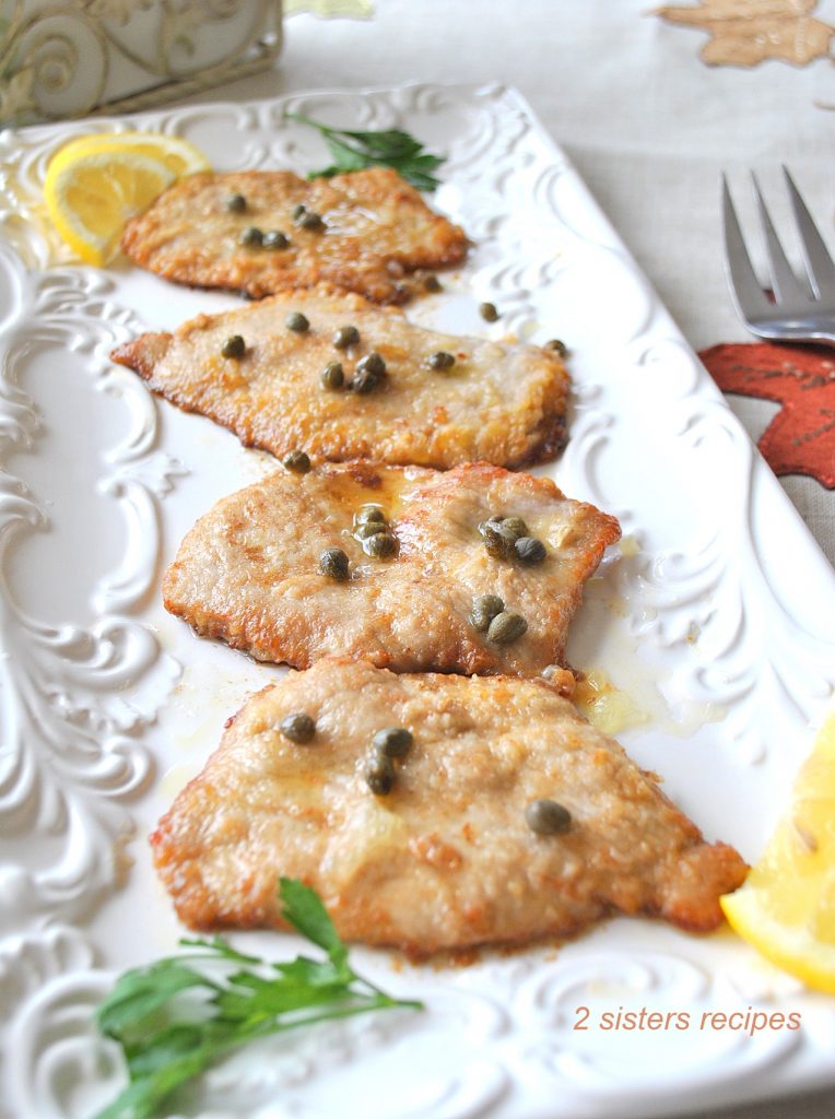 Four pieces of cooked veal with capers on top served on a white platter.