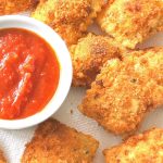 A plate filled with fried ravioli and a small bowl filled with tomato sauce for dipping.