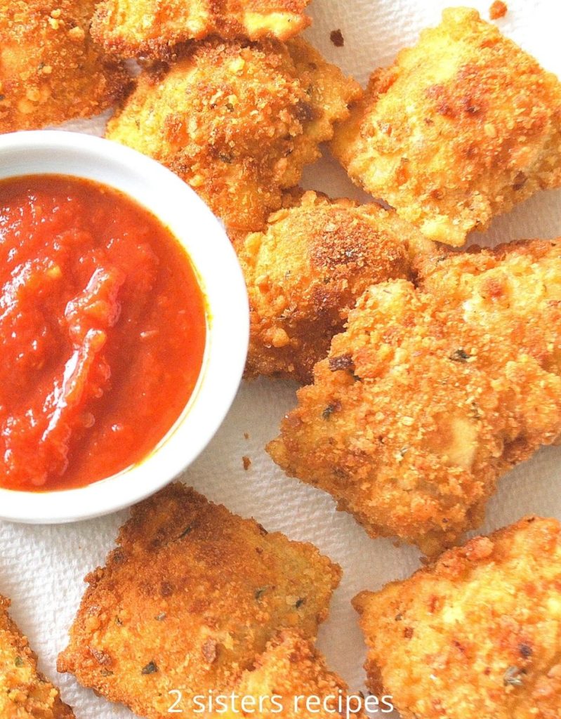 A plate filled with fried ravioli and a small bowl filled with tomato sauce for dipping.  