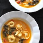 Two bowls filled with tortellini soup with broth and Swiss chard.