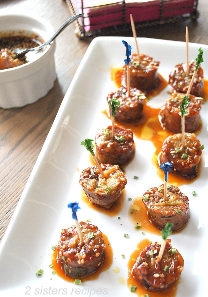 Appetizer size sausage bites with toothpicks on a white serving platter.