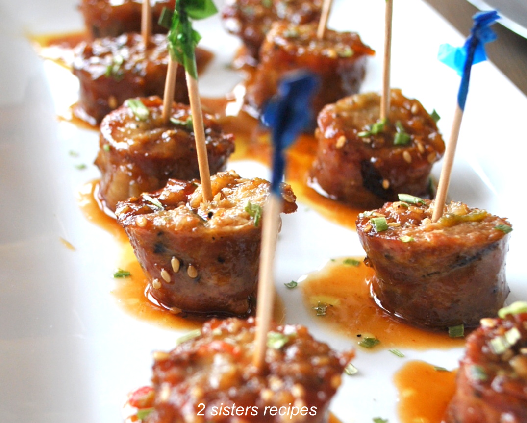 A white serving platter filled with sausage bites with toothpicks in each one.