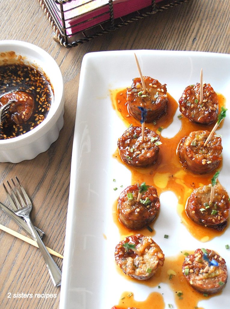 A white platter filled with sausage bites with cocktail toothpicks inserted.