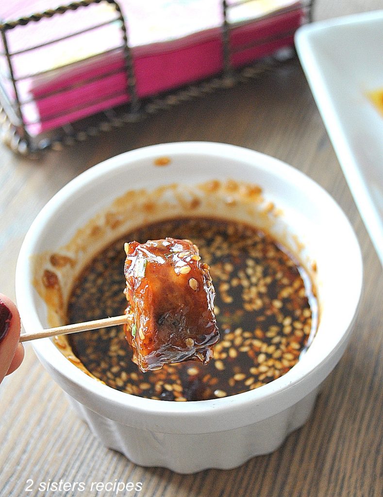 One Sausage Bite is dipped into a white bowl with Sweet & Sour Sauce. 