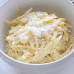 A bowl filled with cooked broken spaghetti with creamy cauliflower and grated cheese on top.